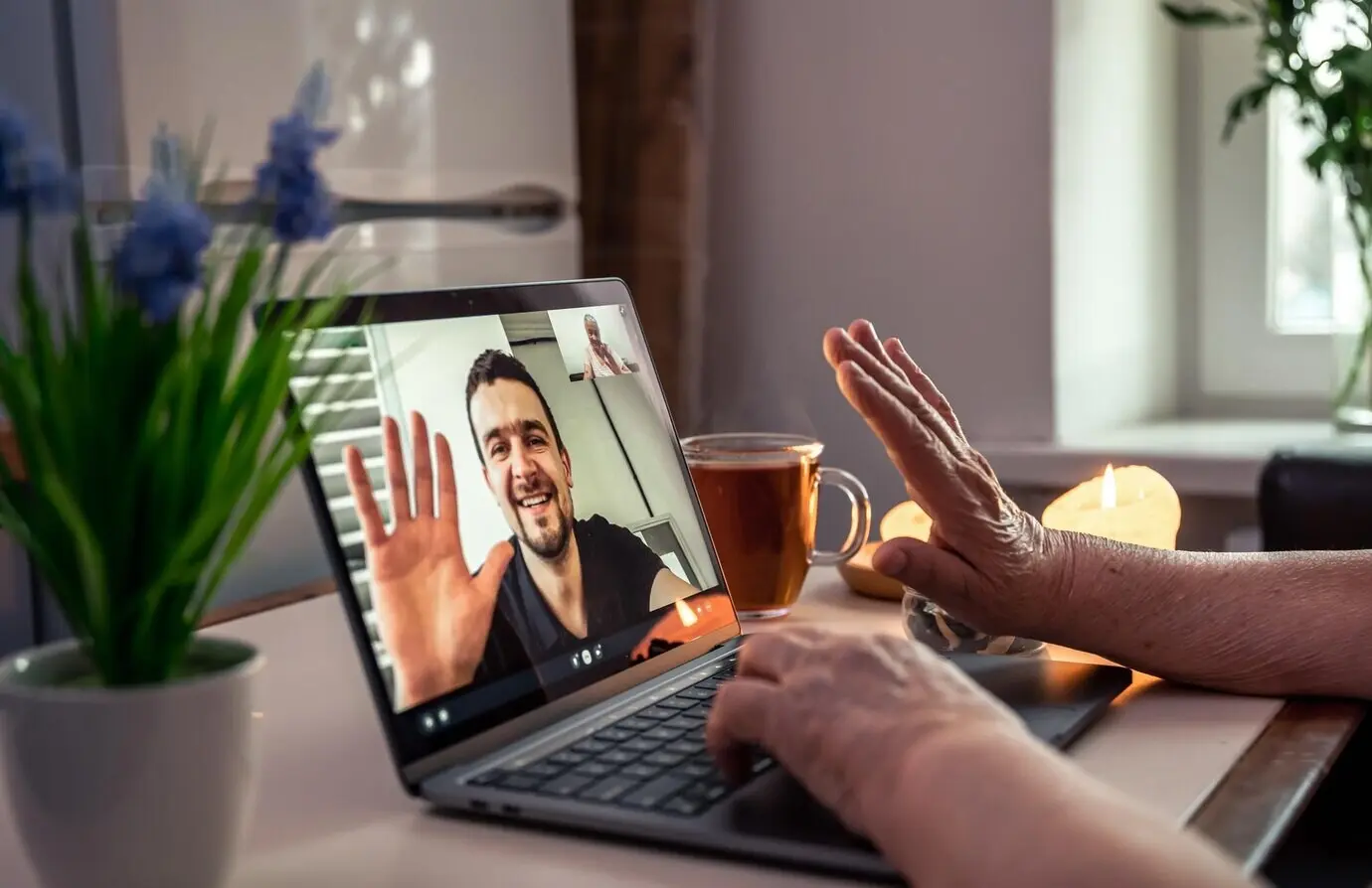 An elderly woman talks to her son over a video call on a laptop.